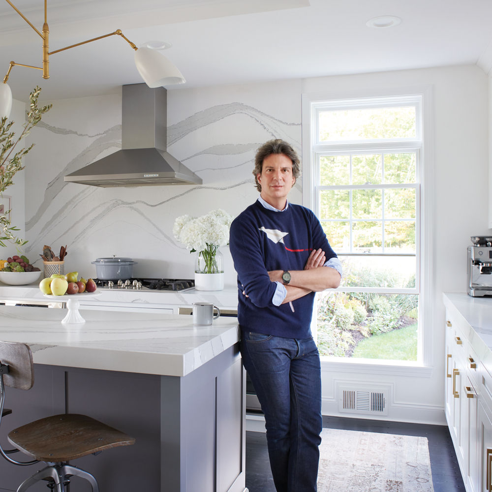 Adam Glassman standing in a white kitchen, leaning against an island with a white quartz countertop.