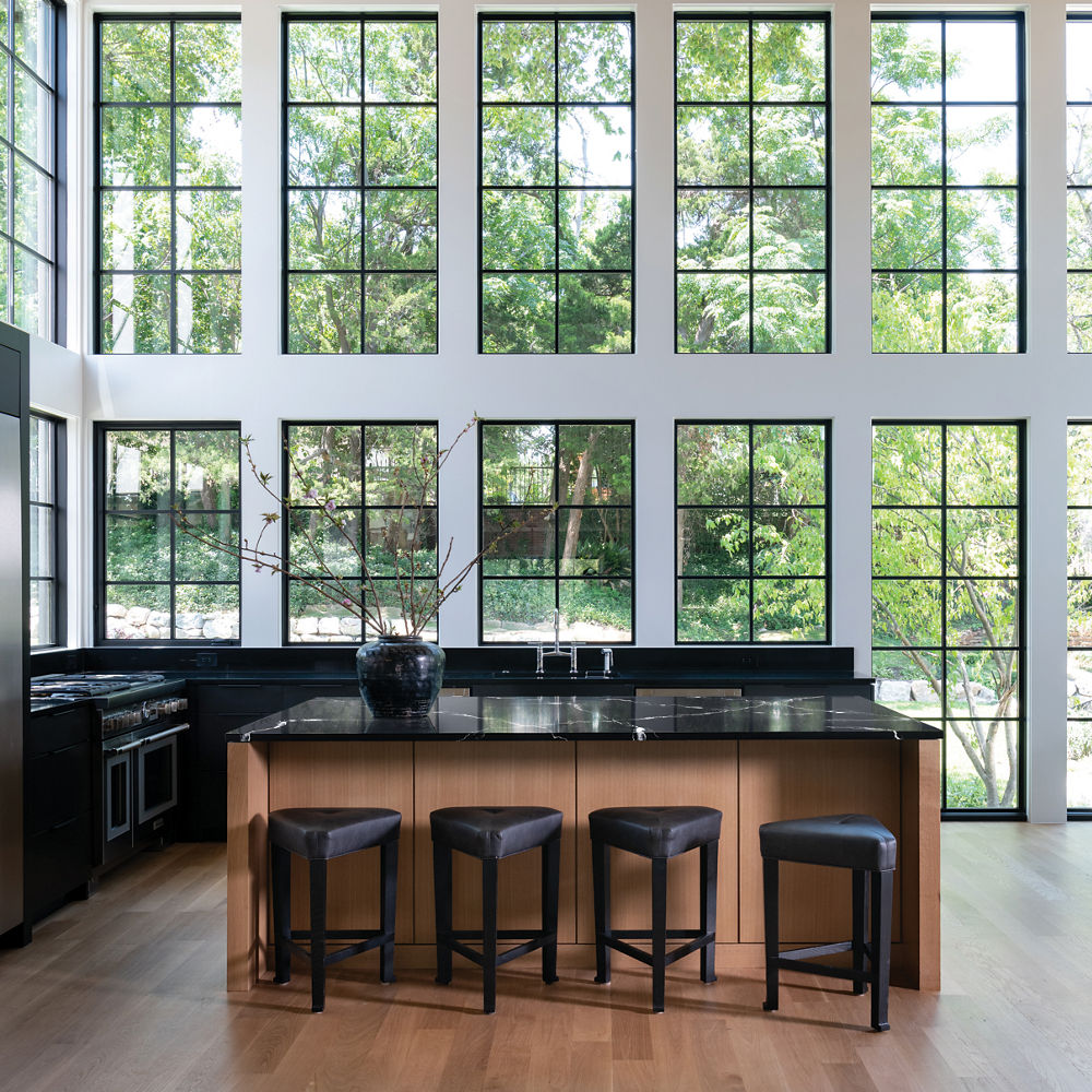 A modern kitchen with tall ceilings, black cabinets topped with black quartz countertops, a center island topped with black and white veined quartz countertops.