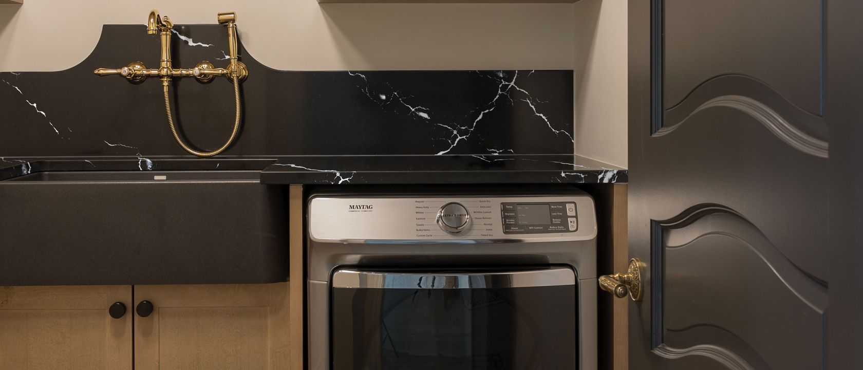 Laundry room with brown cabinets and a washing machine covered by a Cambria Blackbrook Matte quartz countertop.