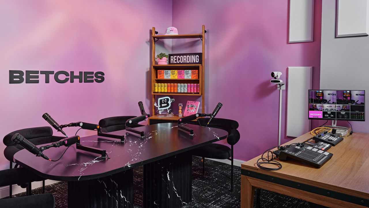 a recording studio with a table topped with black and white veined quartz, purple and pink swirled walls, and several chairs and microphones near the table.