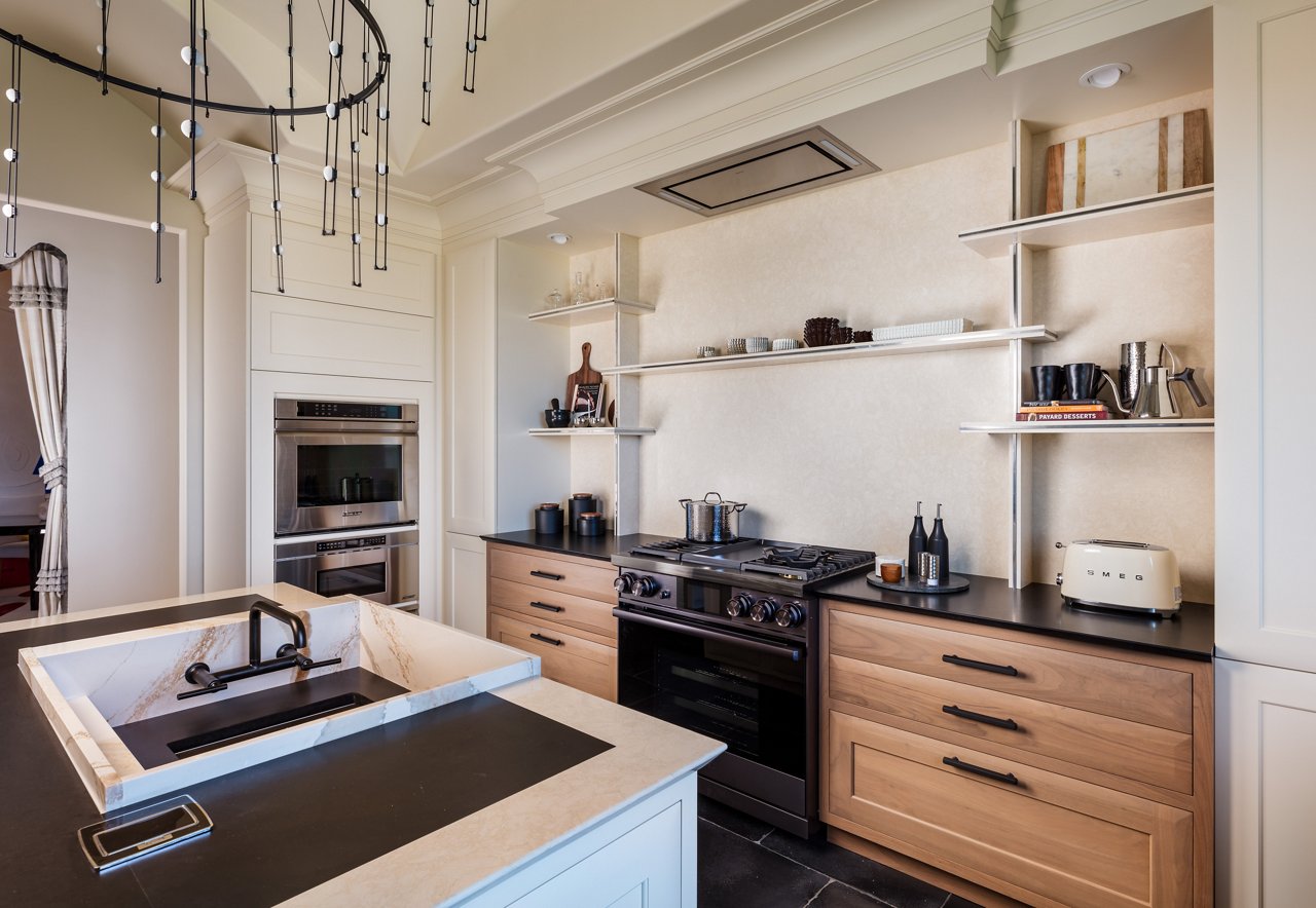 a modern kitchen with oak lower cabinets, white quartz backsplash and custom quartz shelving, a large sink in the island, and black accents throughout. 