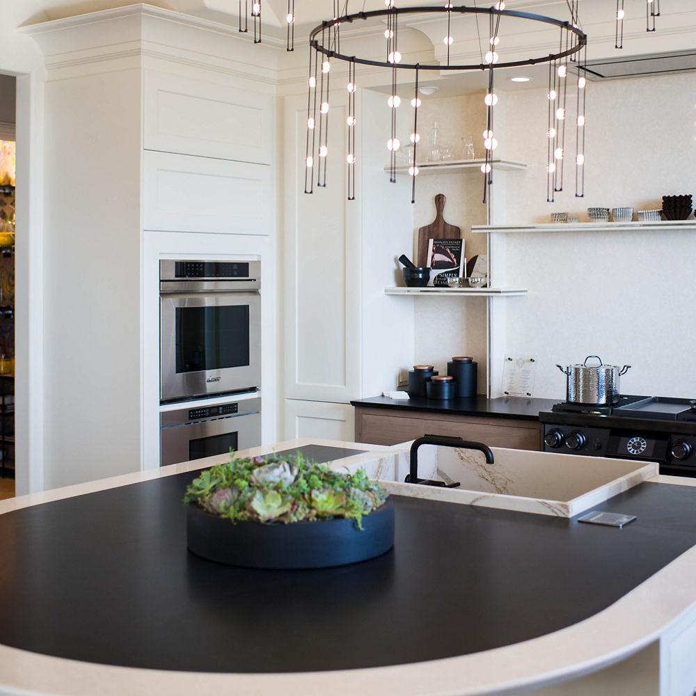 Kitchen with a chandelier hanging over an island with a Cambria Blackpool Matte quartz countertop with a Fairbourne perimeter and Brittanicca Gold Warm sink surround.