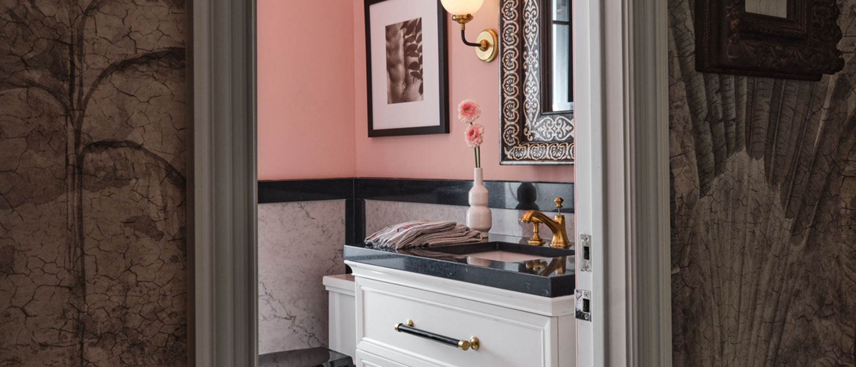 A bathroom with black and white tile flooring, pink painted walls, white cabinets, and black quartz countertops.