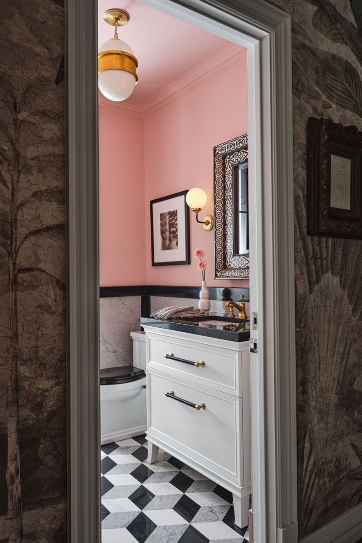 A bathroom with black and white tile flooring, pink painted walls, white cabinets, and black quartz countertops.