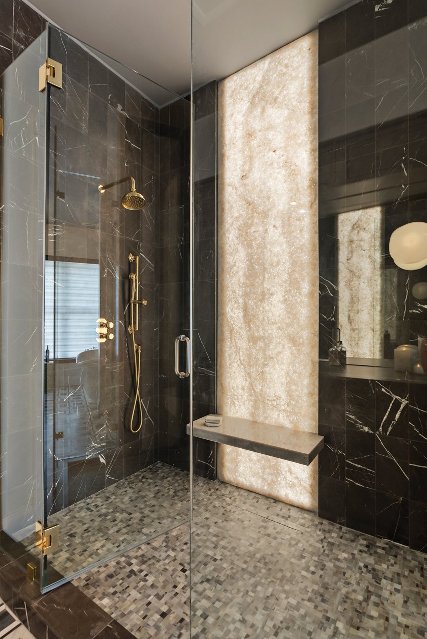 A beautiful kitchen with white cabinets, center island with double waterfall edge and topped with a white quartz countertop with bold veining, matching quartz backsplash, large black hood over the range, and gold accents throughout. 