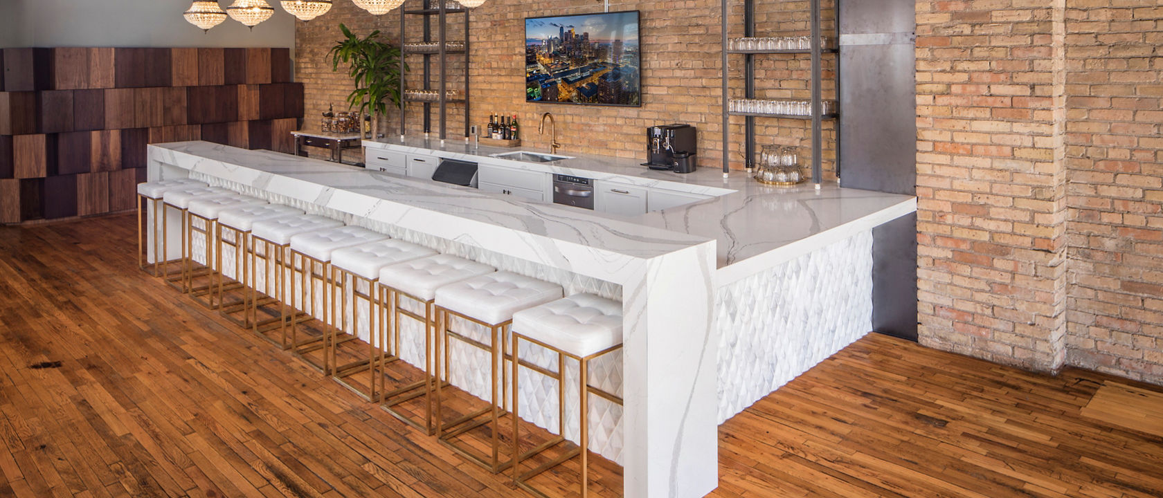 A white bar counter with ten stools sitting in front of the counter surrounded by wooden flooring and brick siding.