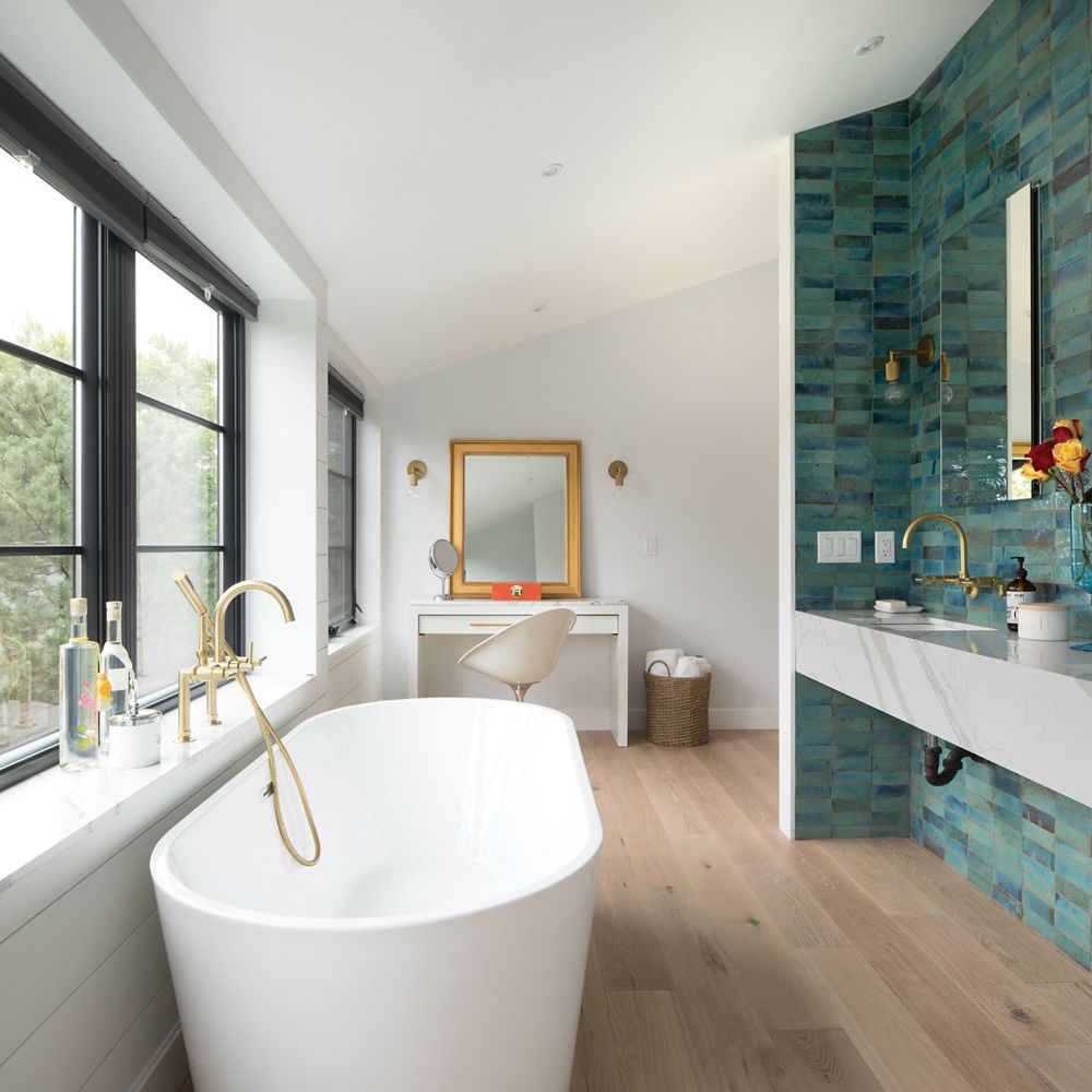 a stunning bathroom with a stand-alone tub, floating quartz vanity with a teal tile backsplash, and large windows.