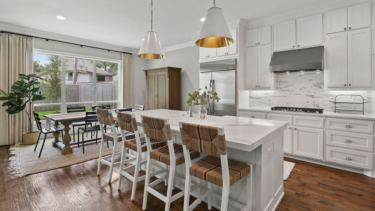 Four white and brown chairs are placed in front of a kitchen island with Cambria Brittanicca Block quartz countertops.