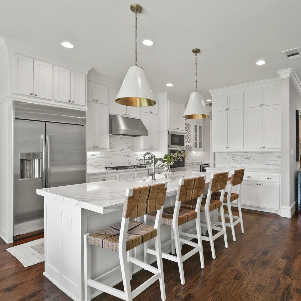 A bright, warm kitchen featuring white cabinets and quartz countertops on its walls, counters, and island.
