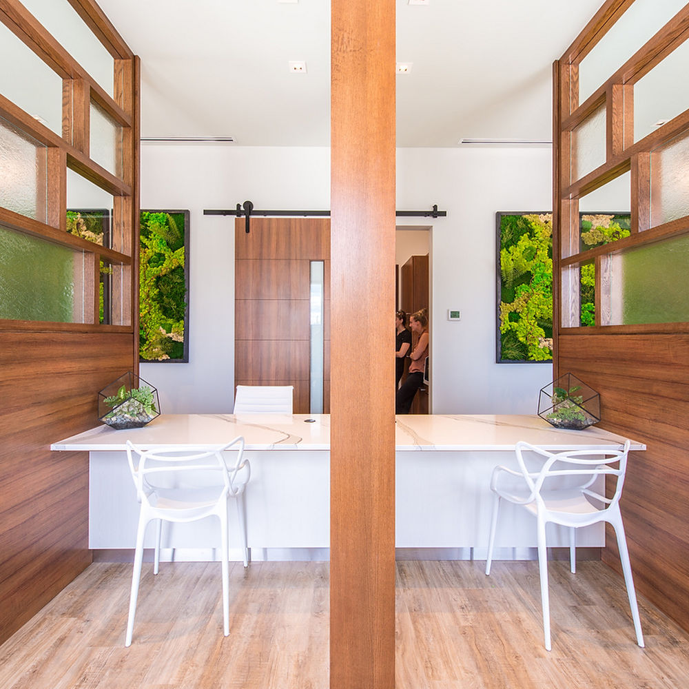 a room with wooden floors, wooden privacy dividers on either side of a desk topped with white quartz countertops and 3 chairs around it