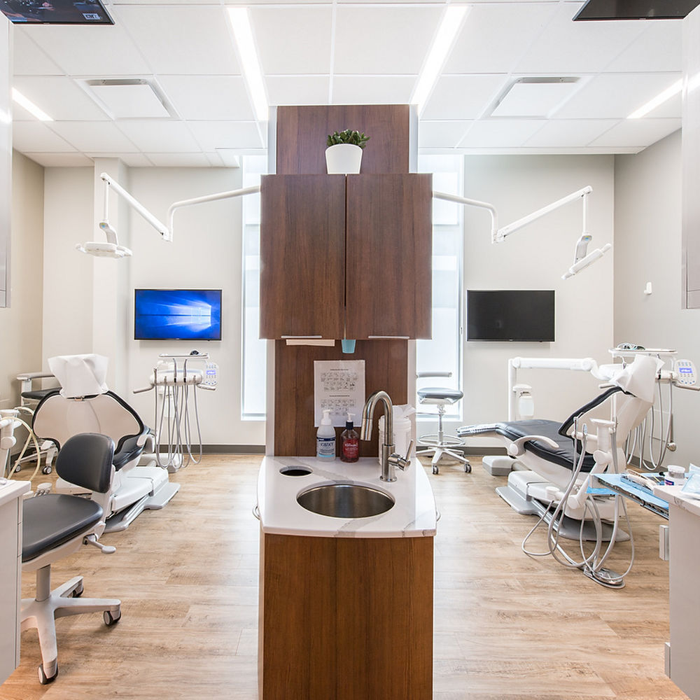 two dental office cleaning rooms separated by a wooden divider with wooden cabinets attached and small sink topped with quartz countertops at the end. 
