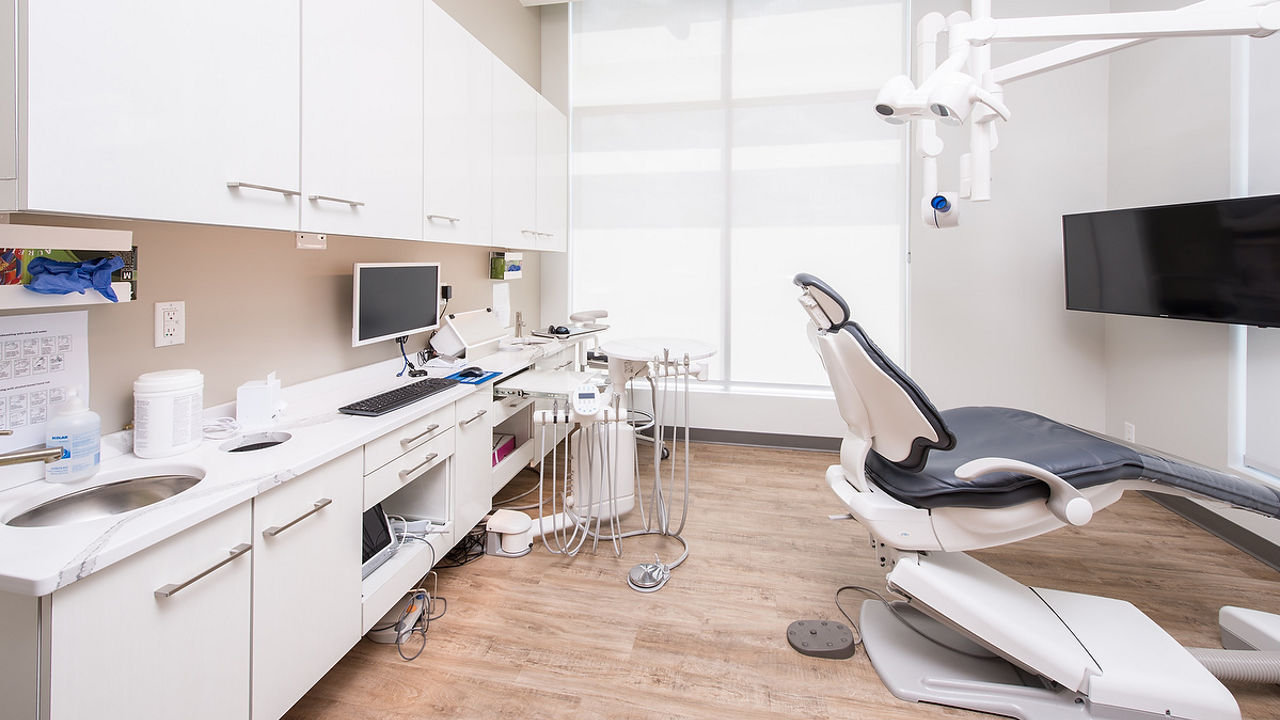 a cleaning room with white lower and upper cabinets, topped with white quartz countertops, a small sink, white walls, and a small flat screen tv in the corner.