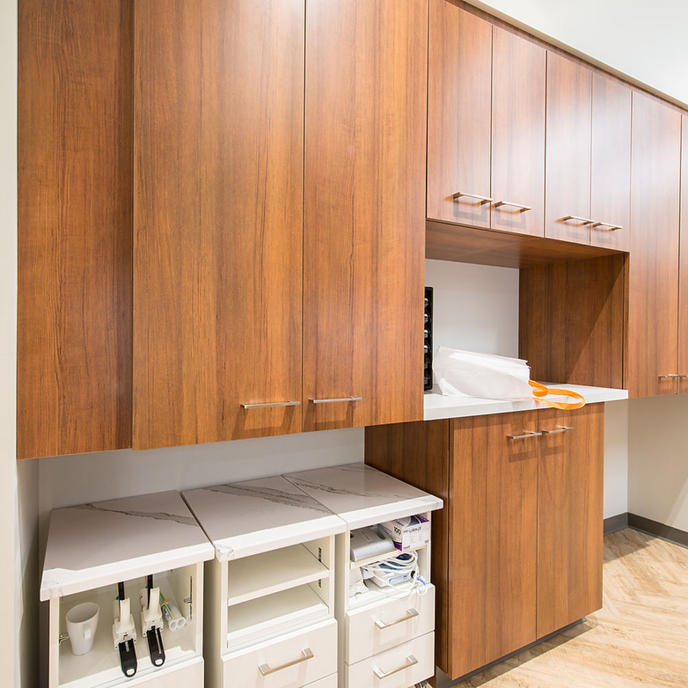 a dental office storage area with oak upper cabinets, and white lower cabinet drawers topped with white quartz countertops.