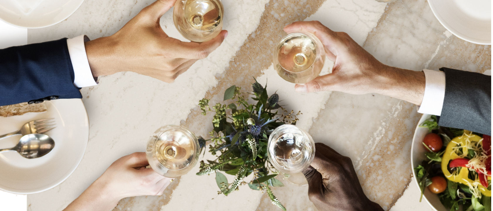 Top-down view of five people holding various drinks over a Cambria Brittanicca Gold Warm quartz countertop.