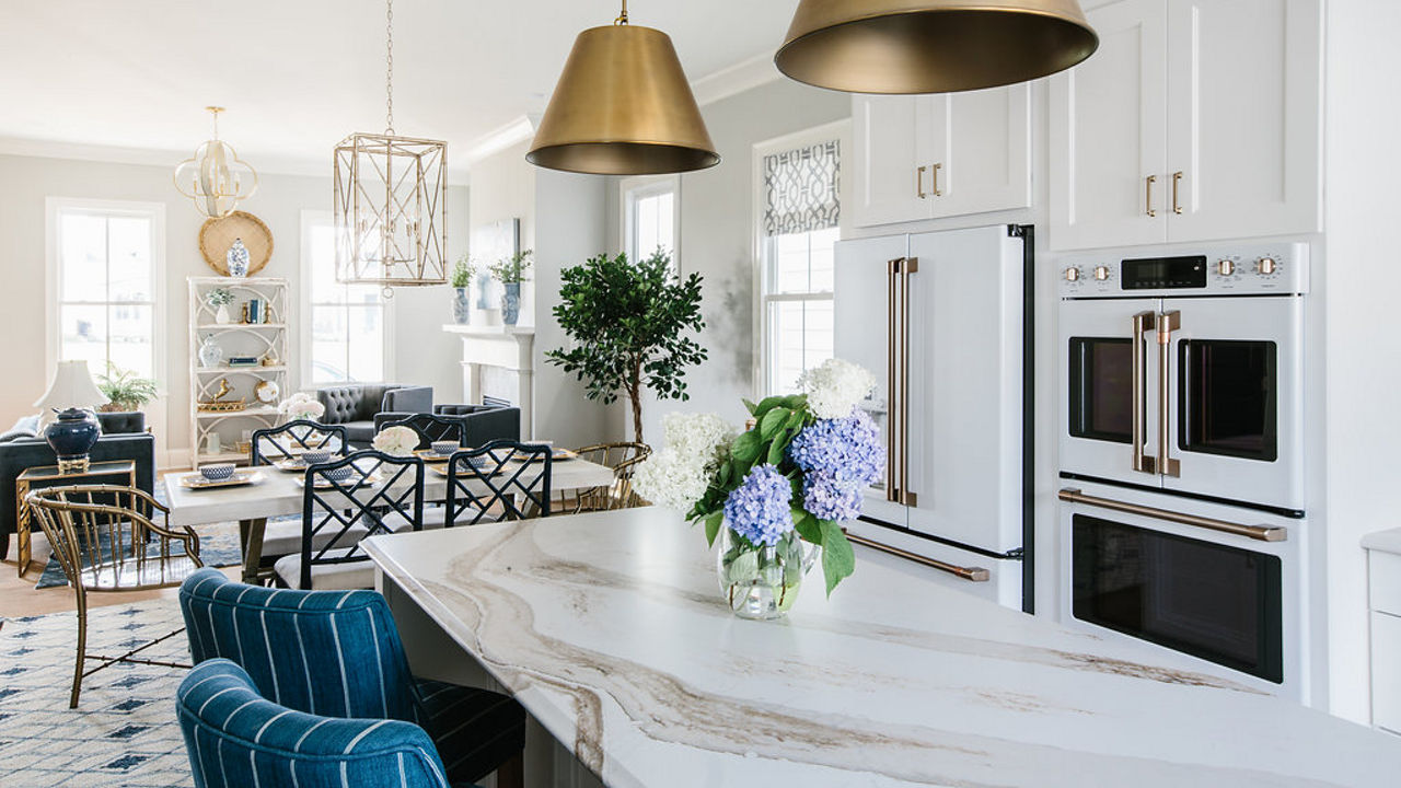 a traditional kitchen with white cabinets, white veined quartz countertops on the island, teal barstools, and matte gold light fixtures and hardware.