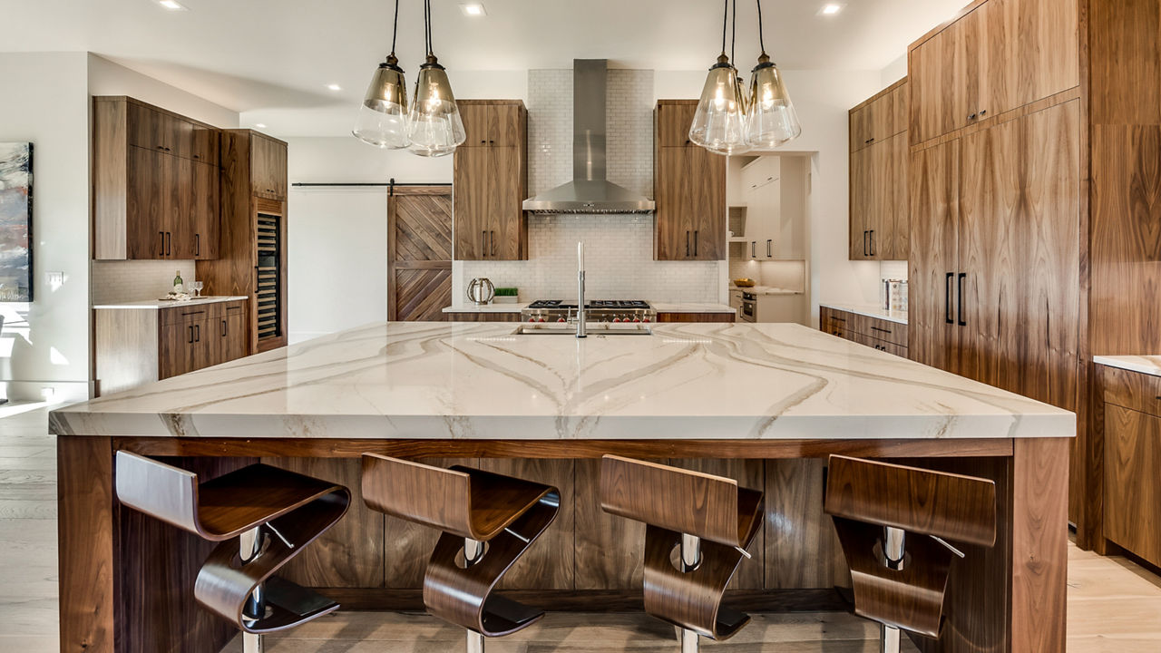 A large kitchen with brown oak cabinets and chairs and Brittanicca Gold Warm quartz countertops