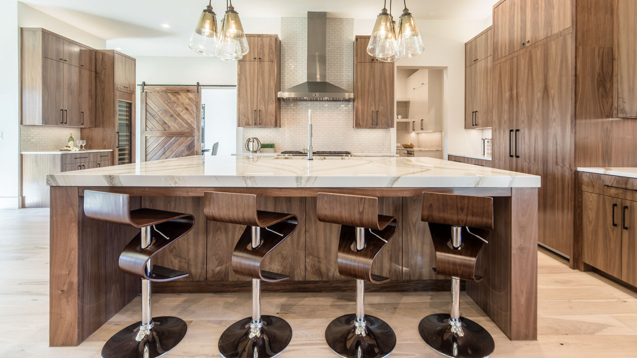 a large kitchen with oak cabinets, matching swivel bar stools, white veined quartz countertops, a large range and hood, and a barn door.