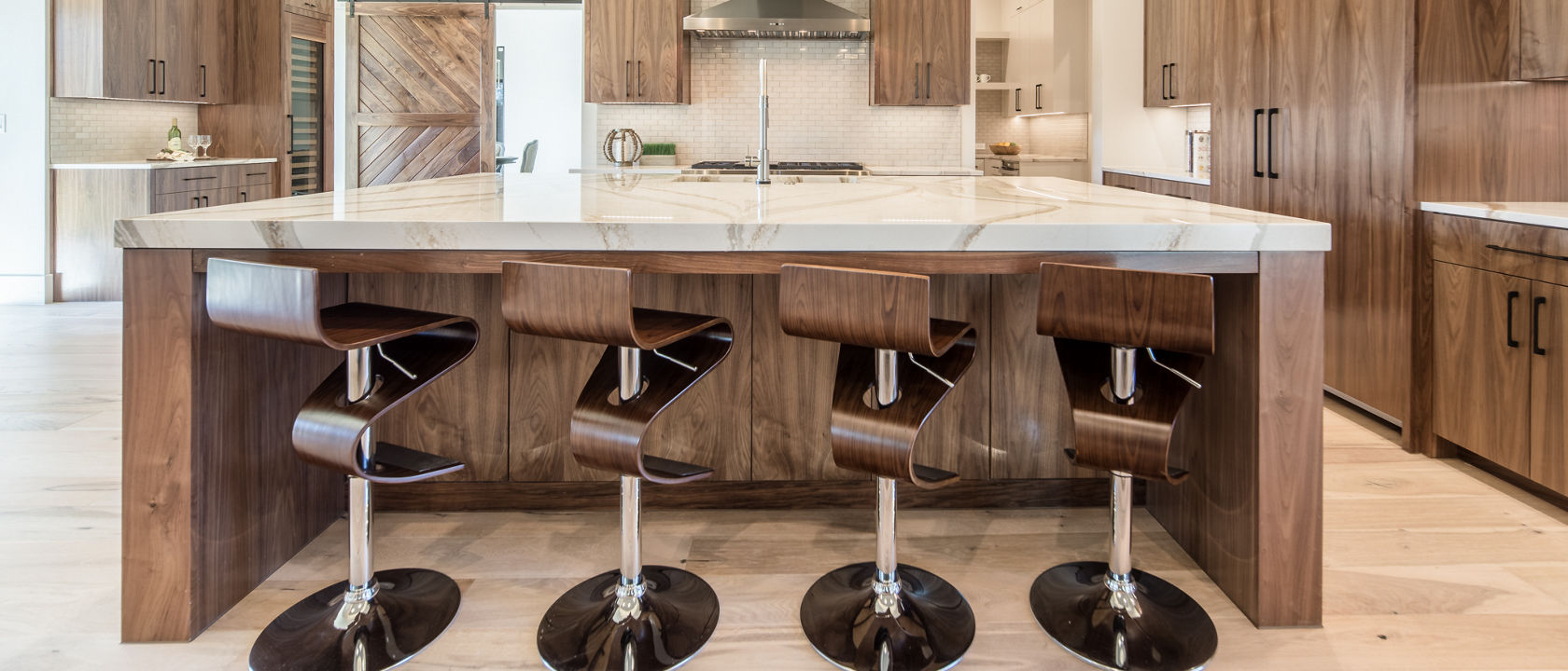 a large kitchen with oak cabinets, matching swivel bar stools, white veined quartz countertops, a large range and hood, and a barn door.