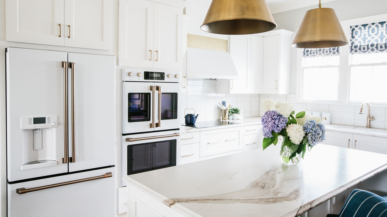 A white kitchen with gold fixtures and Brittanicca Gold Warm quartz countertops 