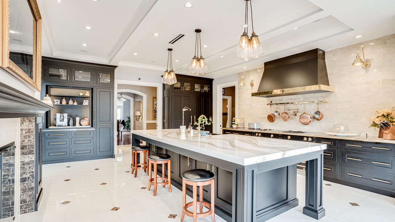 A luxury kitchen with black cabinets and gold fixtures with Brittanicca Gold Warm quartz countertops