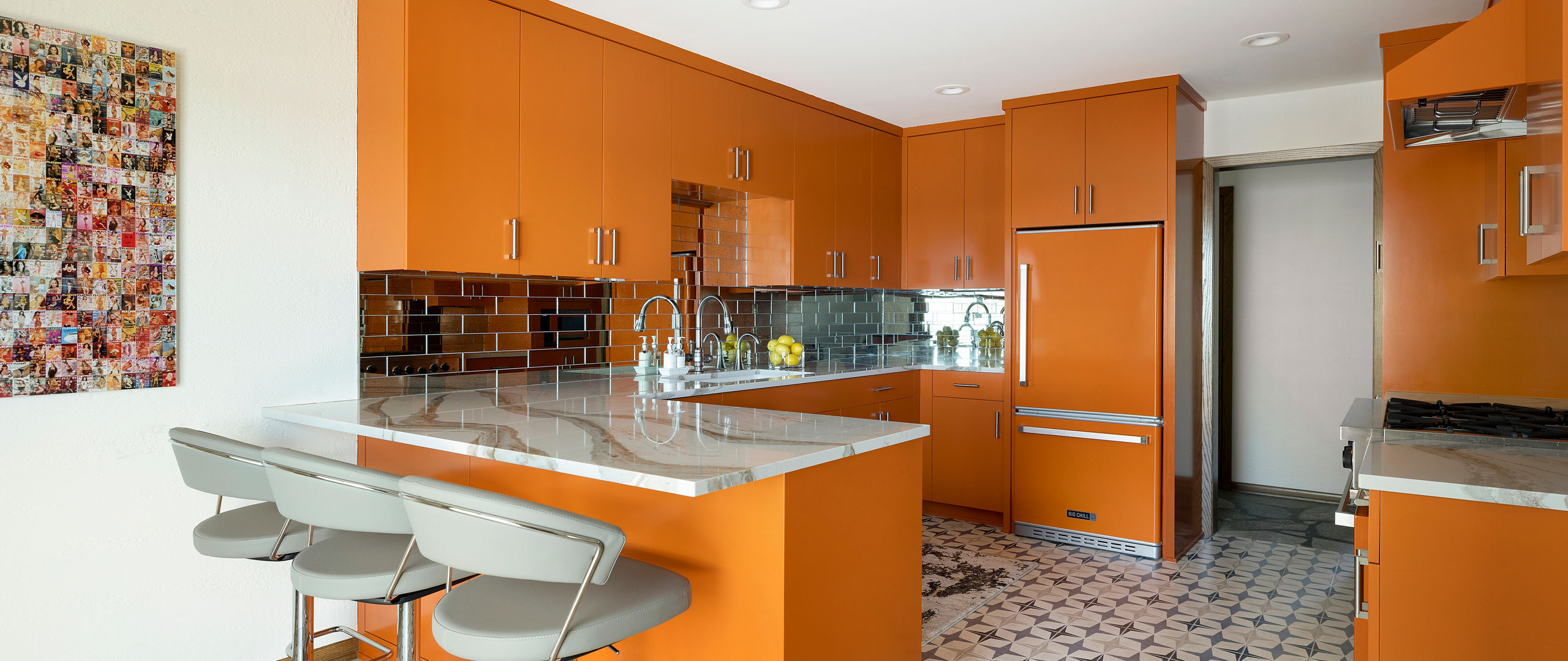 a bold orange kitchen with tiled flooring, white veined quartz countertops, a shiny black tile backsplash and three gray bar stools