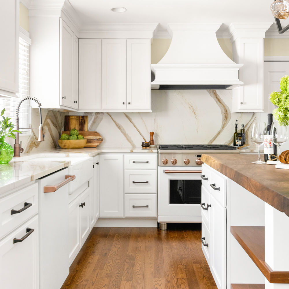 A kitchen with white cabinets and a butcher block countertop with a Brittanicca Gold Warm backsplash