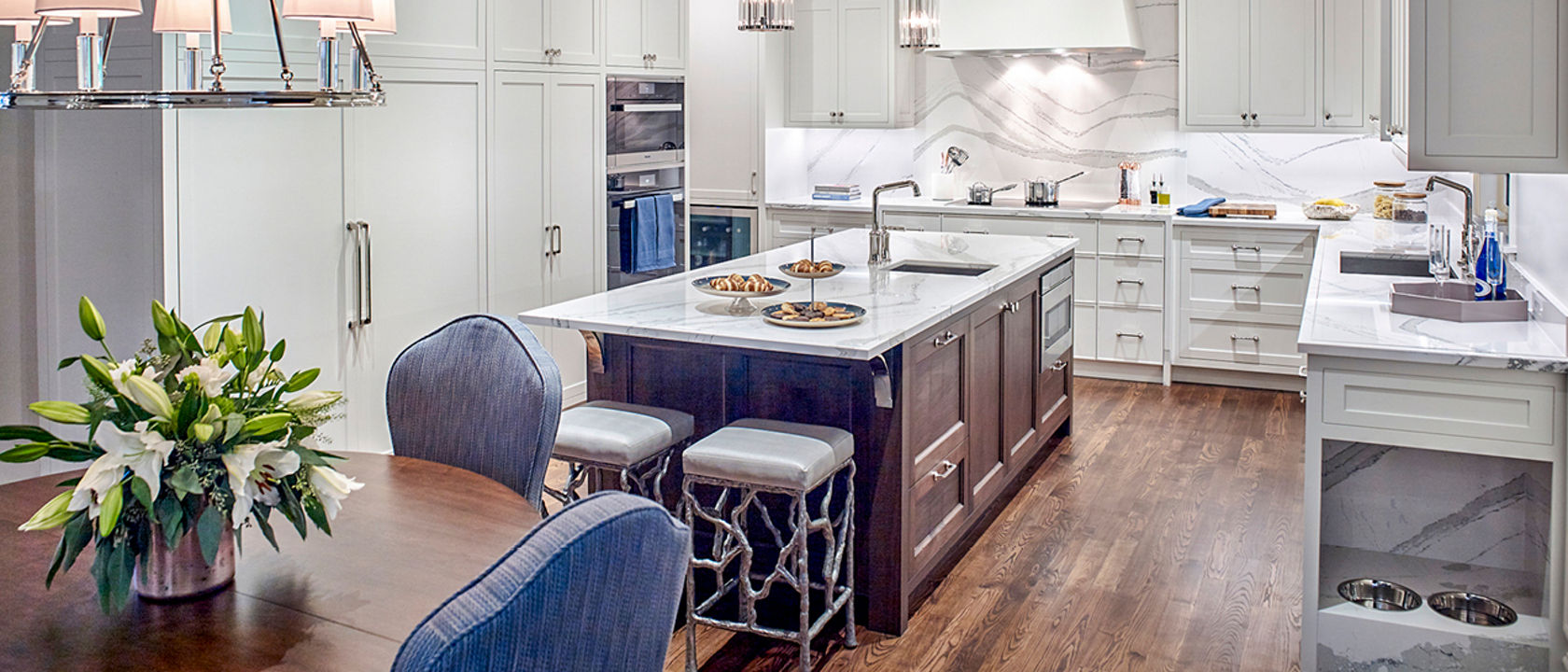 a gorgeous kitchen with white quartz countertops and matching backsplash, white cabinets, and modern appliances with a built in dog food station.