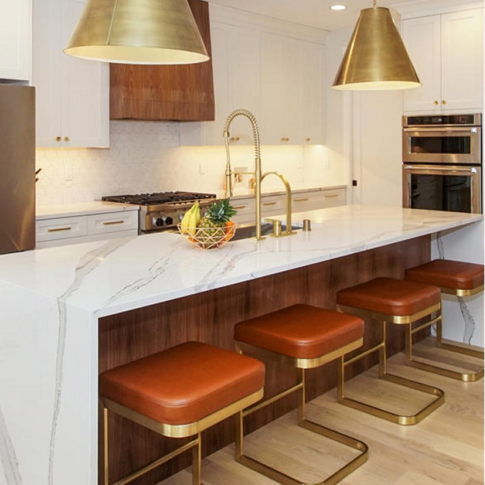 Warm kitchen with a counter and island featuring Cambria Brittanicca quartz countertops and siding. The kitchen blends a white and amber color palette.