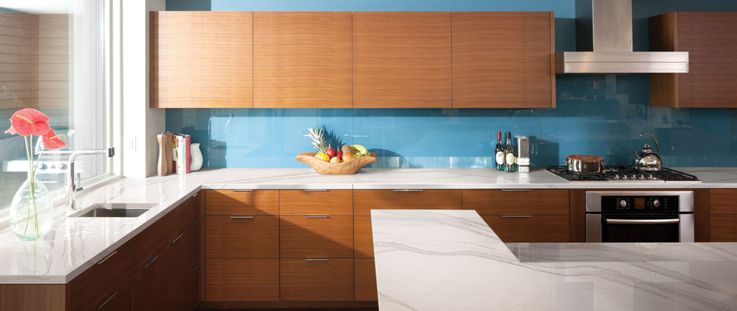 a mid-century modern kitchen with wooden cabinets, a blue backsplash, and white quartz countertops.