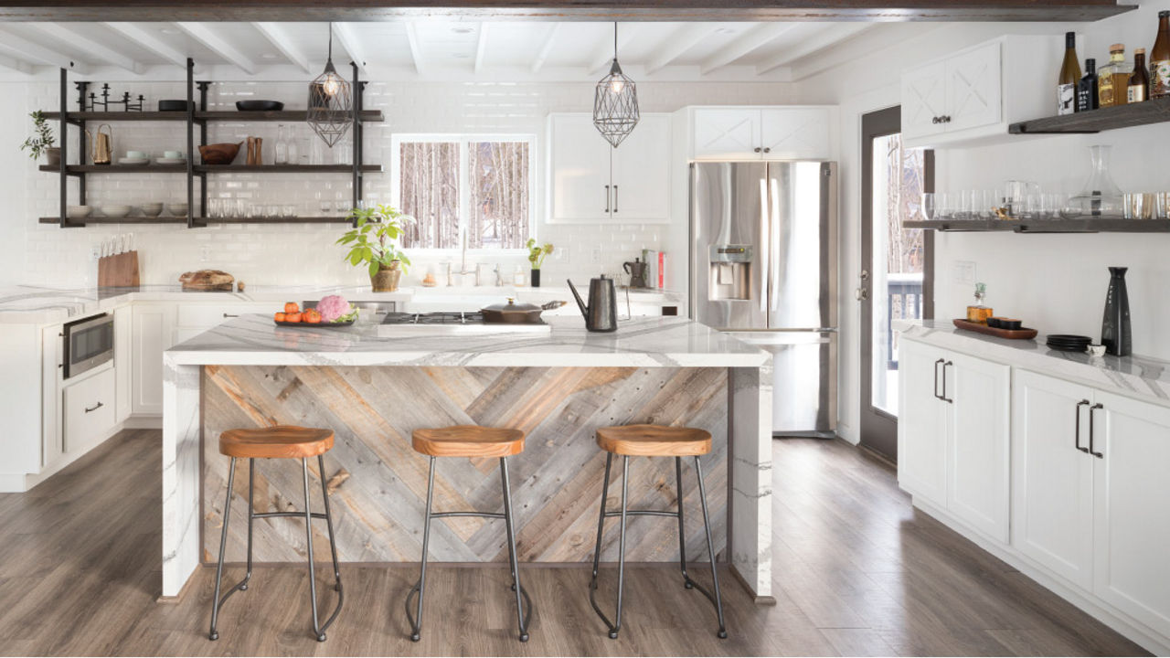 a gorgeous kitchen with white cabinets, a double waterfall island topped with white veined quartz countertops, a fun herringbone pattern on the inside of the island, three barstools, and a subway tile backsplash.