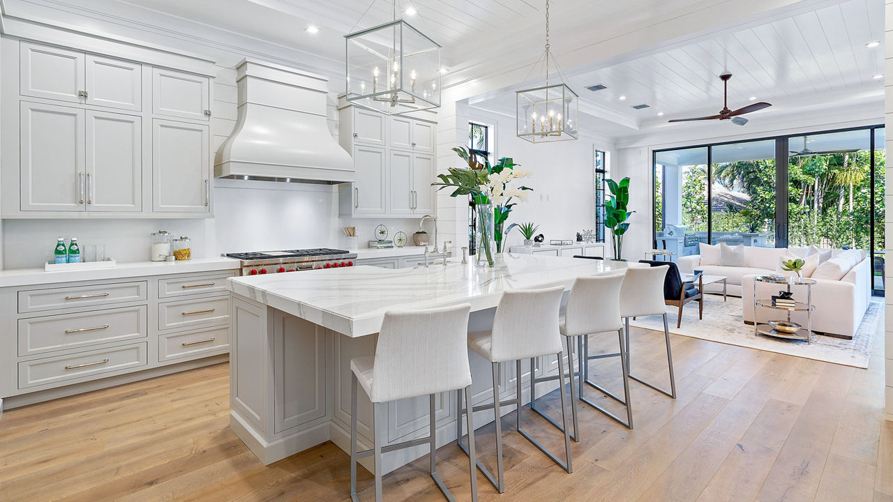Kitchen with a white color palette with its white chairs and counter and island with Cambria Brittanicca quartz countertops.