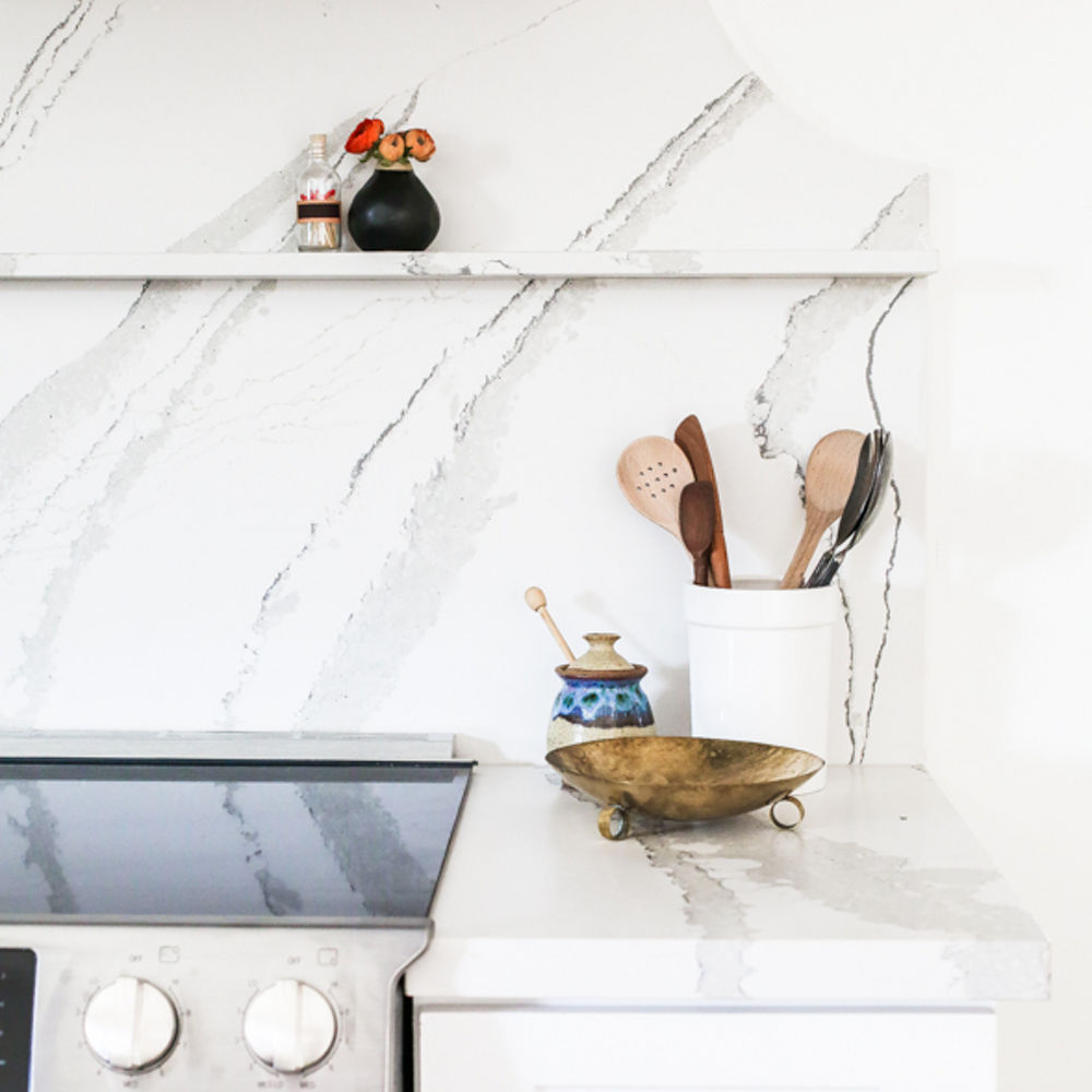 A white veined quartz countertop and matching backsplash and shelf and white cabinets. 
