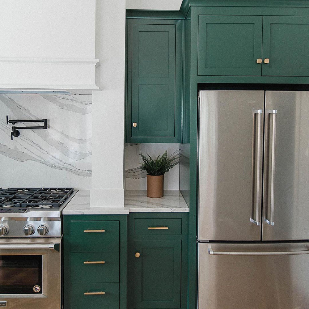 A kitchen with emerald green cabinets, white quartz countertops and backsplash, and stainless steel apliances.