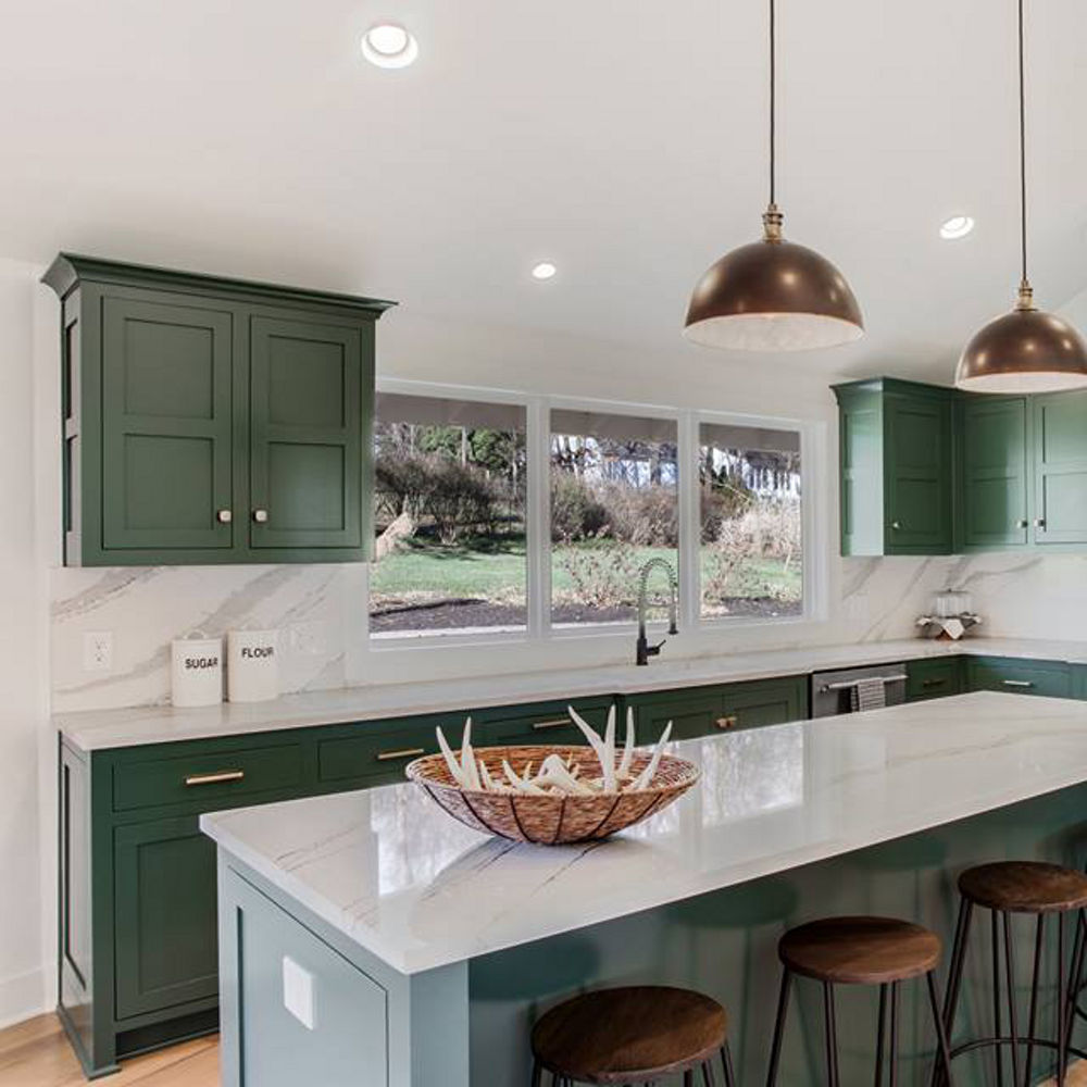A kitchen with emerald green cabinets, white quartz countertops, bronze accents, and wood and metal barstools.
