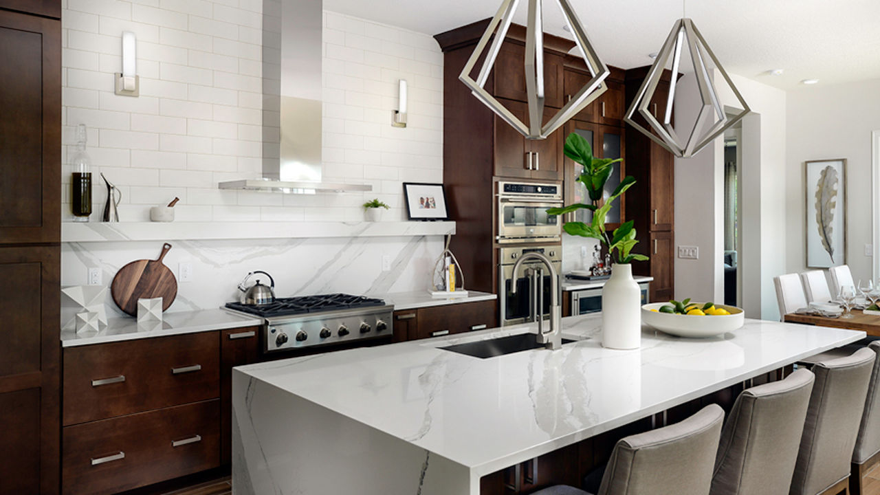 A kitchen with dark wood cabinets and Cambria Quartz Brittanicca waterfall edge kitchen island countertop and matching backsplash.