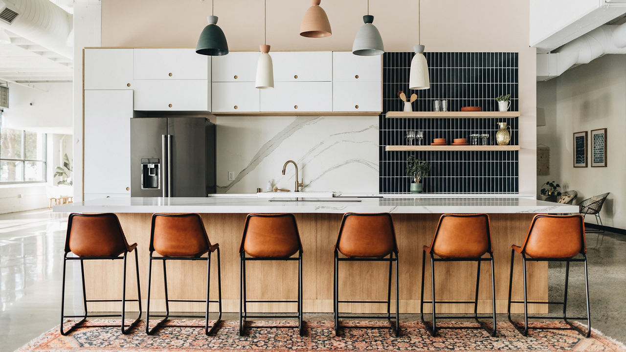 A modern kitchen with white quartz countertops and matching quartz backsplash, white cabinets, open shelving with black tile backsplash behind it, and six leather barstools