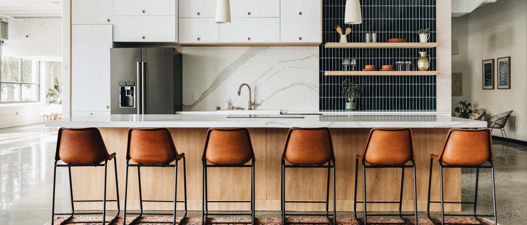 A modern kitchen with white quartz countertops and matching quartz backsplash, white cabinets, open shelving with black tile backsplash behind it, and six leather barstools
