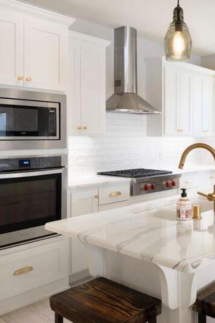 a traditional kitchen with white upper and lower cabinets, white center island topped with Cambria quartz countertops, wooden bar stools surrounding the island, and modern stainless steal appliances.