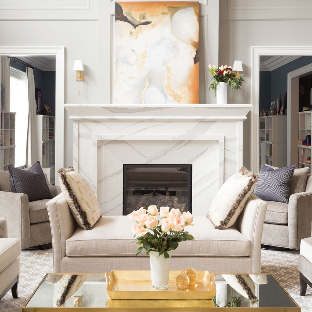 a luxurious living room with a white quartz fireplace, tall ceilings, three organic chandeliers, white furniture, and a coffee table with gold metallic accents.