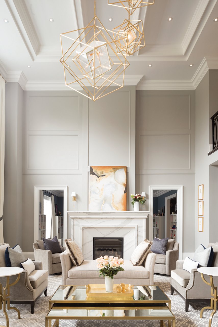 a luxurious living room with a white quartz fireplace, tall ceilings, three organic chandeliers, white furniture, and a coffee table with gold metallic accents.