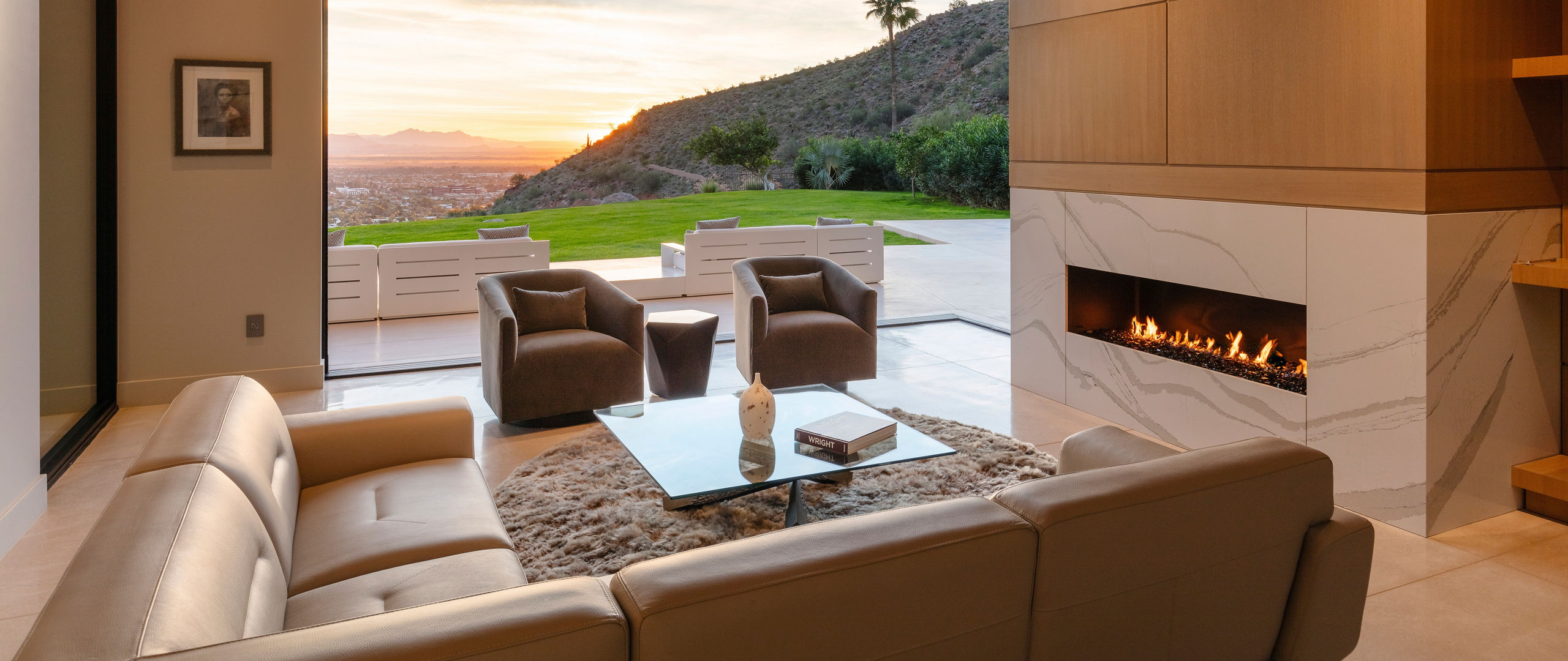 a lounge area with a fireplace made from white veined quartz with a sectional couch, two armchairs, and a large window.