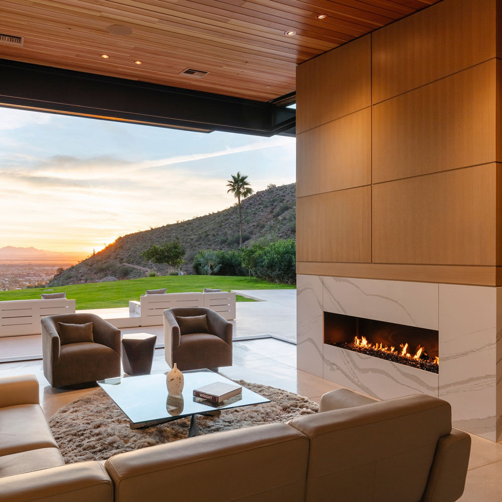 a lounge area with a fireplace made from white veined quartz with a sectional couch, two armchairs, and a large window.