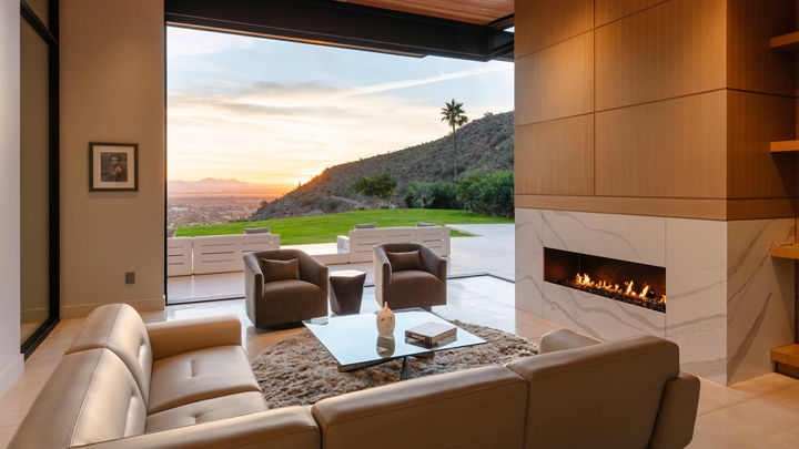 a lounge area with a fireplace made from white veined quartz with a sectional couch, two armchairs, and a large window.