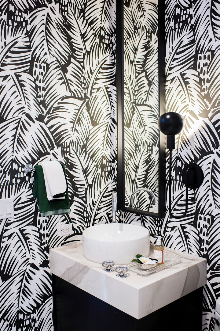 a powder bathroom with black vanity topped with white quartz countertops and a bold black and white leaf wallpaper.