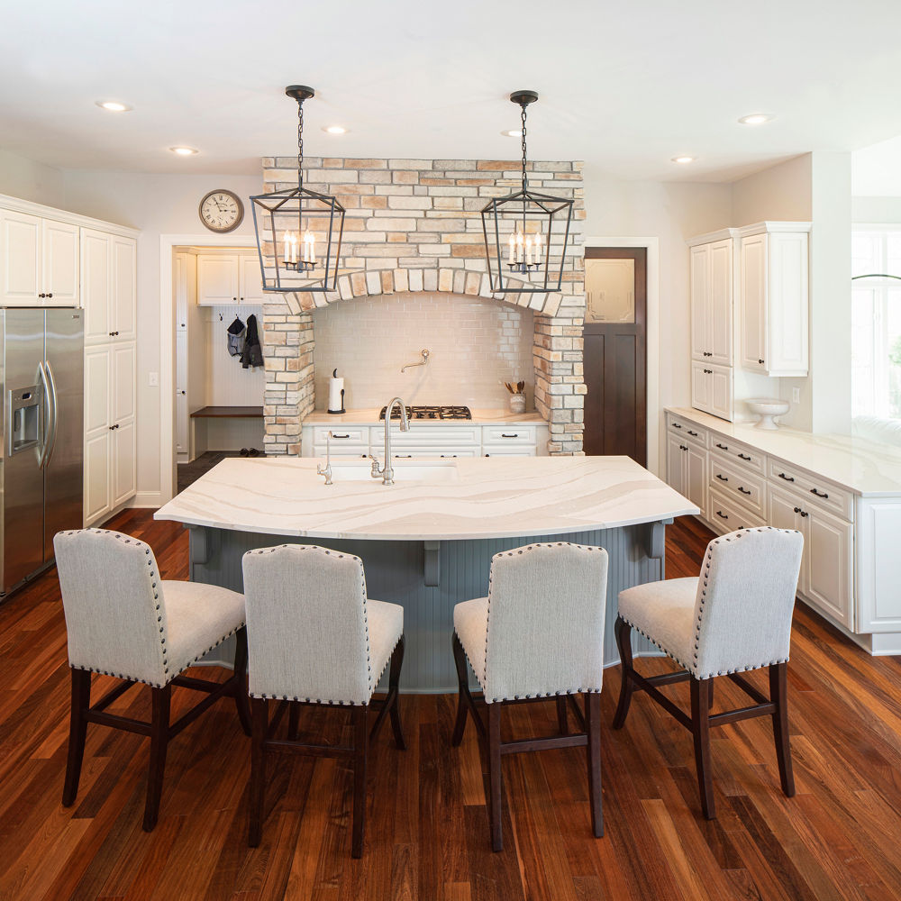 A kitchen with four white chairs in front of a curved island with a Cambria Brittanicca Warm quartz countertop.
