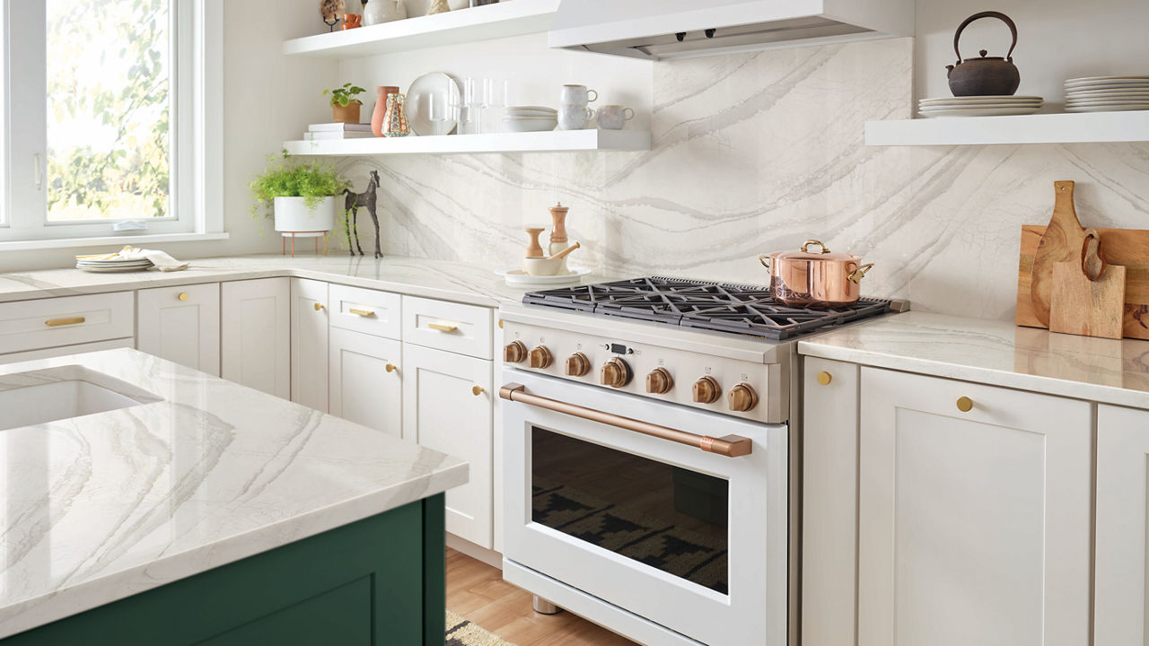 a kitchen with white cabinets, white quartz countertops and backsplash, white hood and range, open shelving, and a green island.