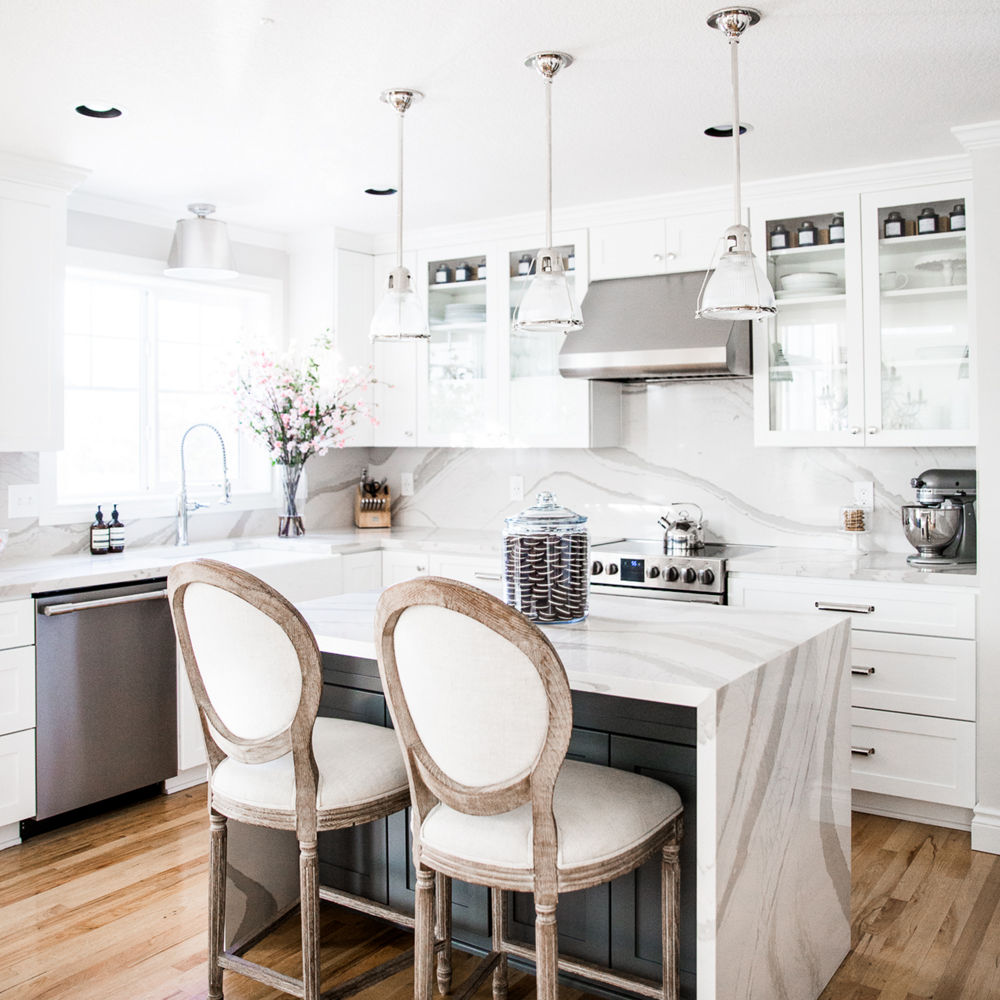 a gorgeous kitchen with white upper and lower cabinets, a double waterfall edge center island topped with white quartz countertops and matching quartz backsplash and countertops.