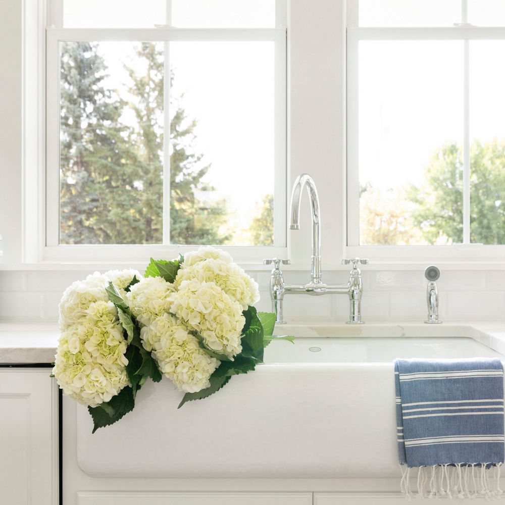 A closeup of a white farmhouse sink with Cambria Brittanicca Warm countertops