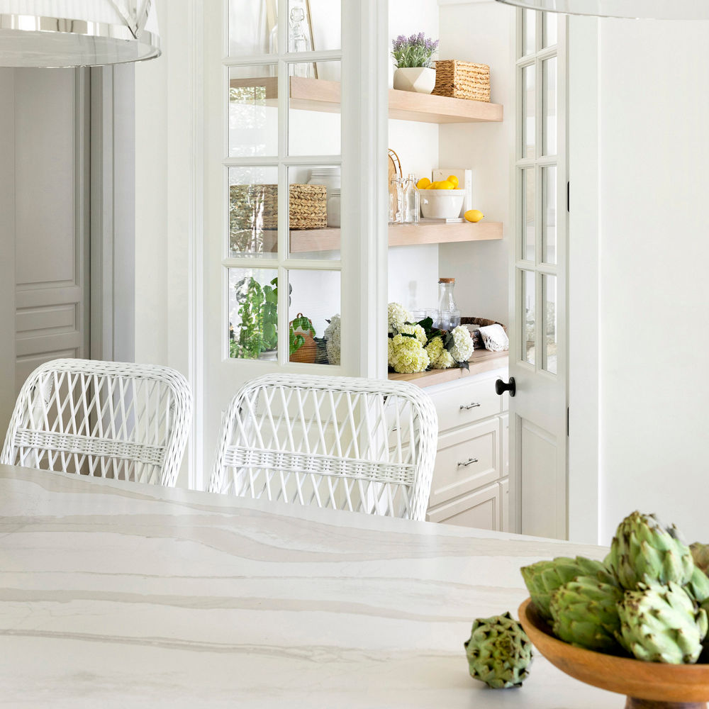 Two white chairs sitting in front of a table with a Cambria Brittanicca Warm Matte quartz countertop.