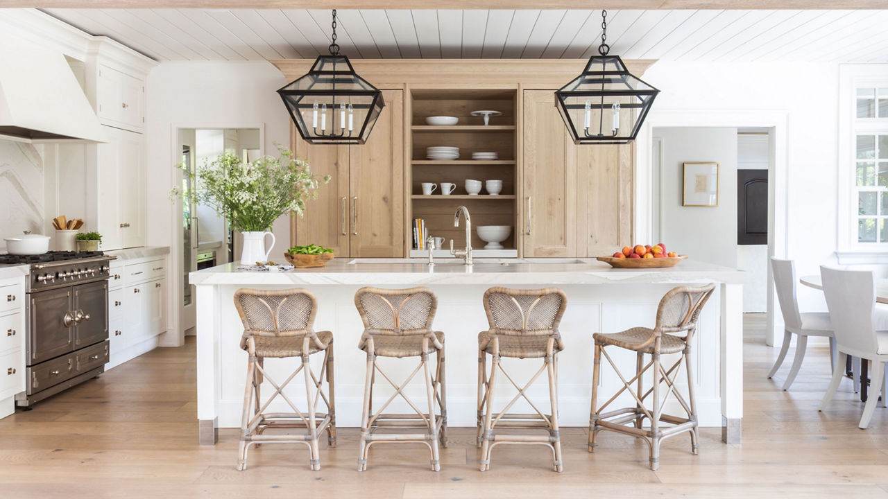 a modern farmhouse inspired kitchen with white and oak cabinets, a modern range and hood, open shelving, a white quartz veined backsplash, countertops, and island, and black pendant light fixtures. 